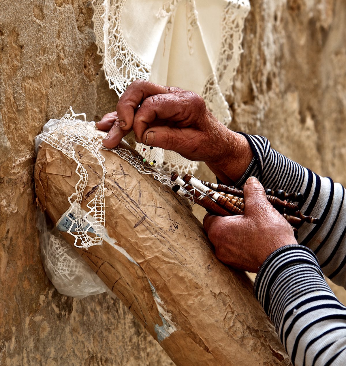 A lacemaker's hands working bobbin lace over a bolster pillow in Malta — the same technique Europe's lace towns share.