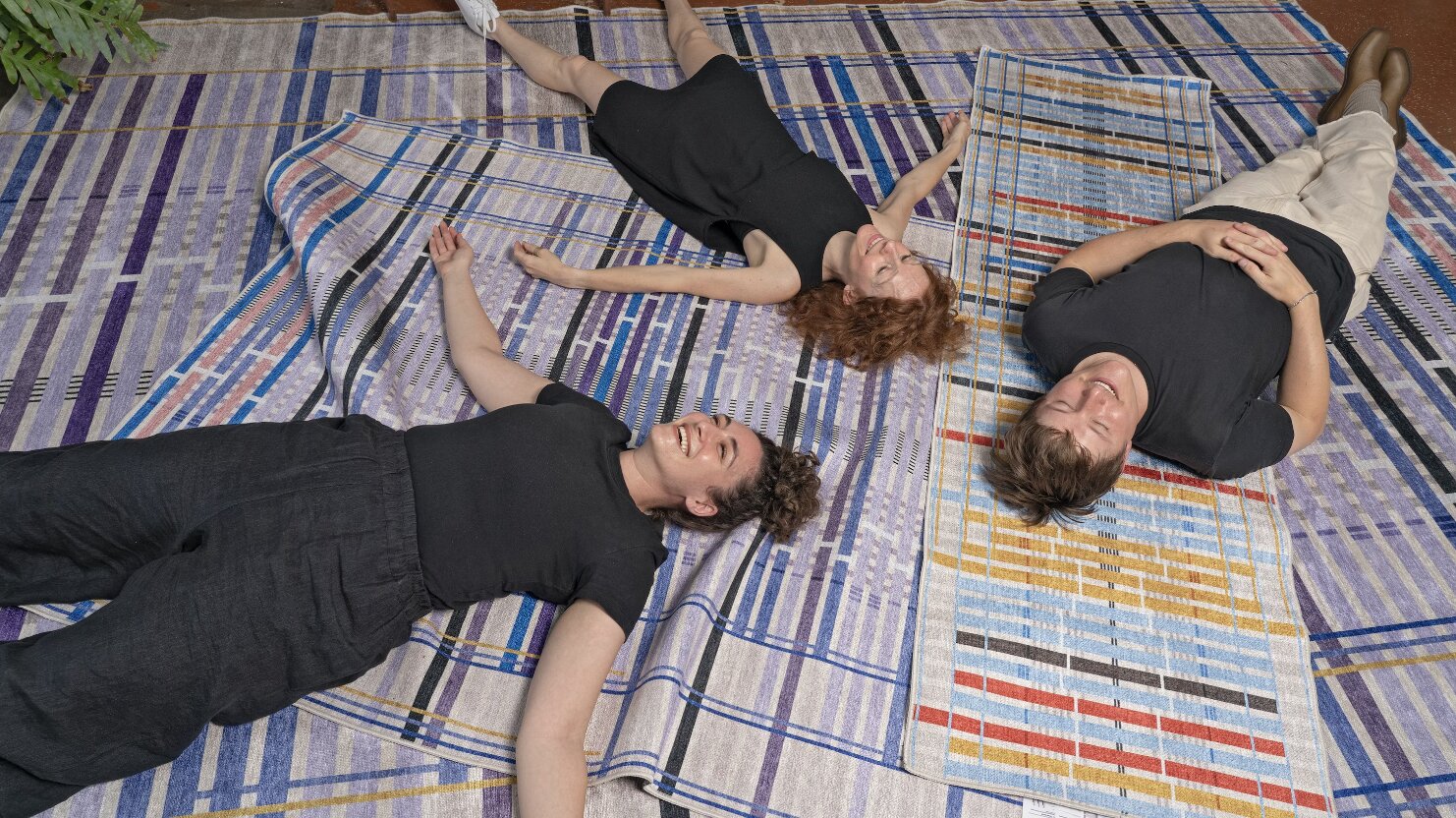 Giorgia Lupi and two collaborators lying on the Unraveling Stories rugs, laughing, photographed from above
